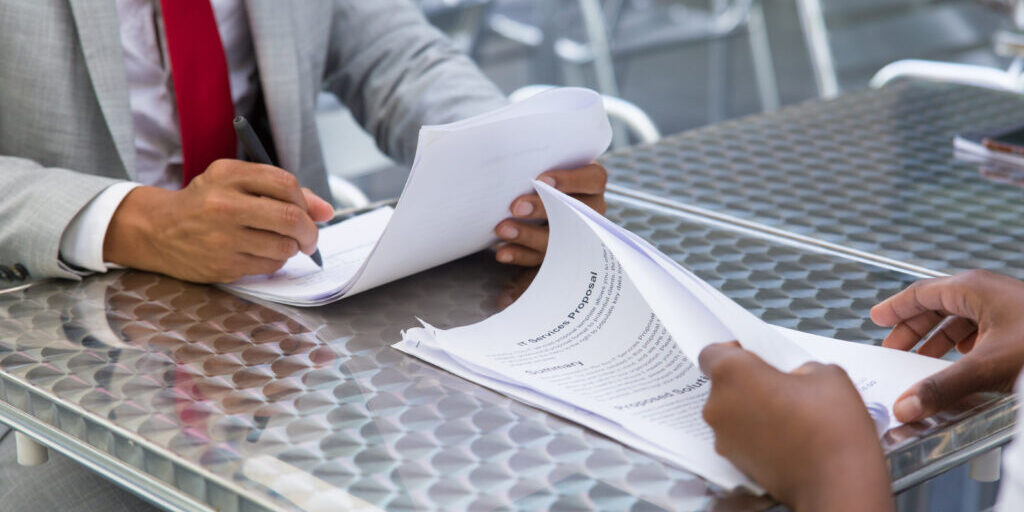 Business partners checking and signing documents in street cafe. Closeup of papers and writing business man hand. Deal or paperwork concept