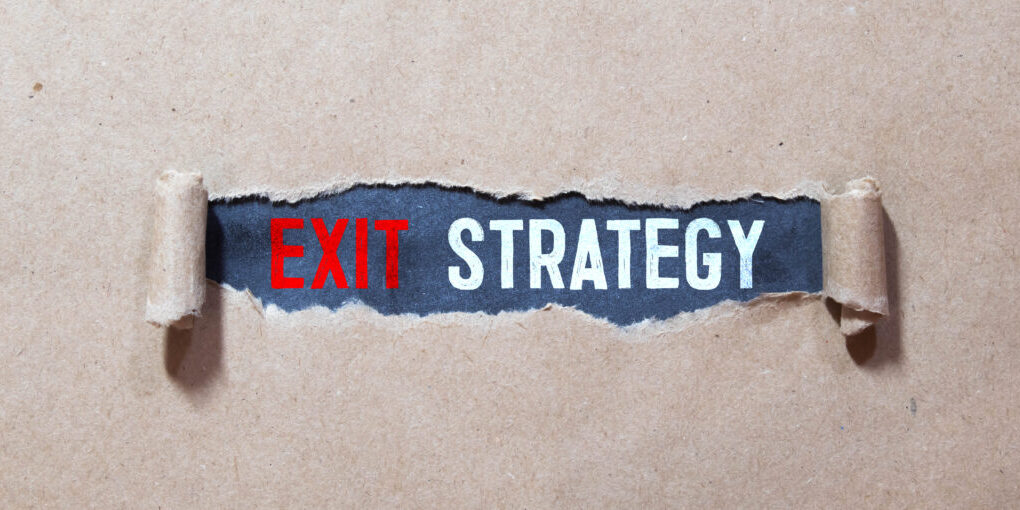 Exit Strategy text with a person holding a pen on a wooden desk.