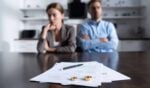 A stressed woman sitting at a table looking over legal documents and financial bills, representing the burden of divorce and debt.